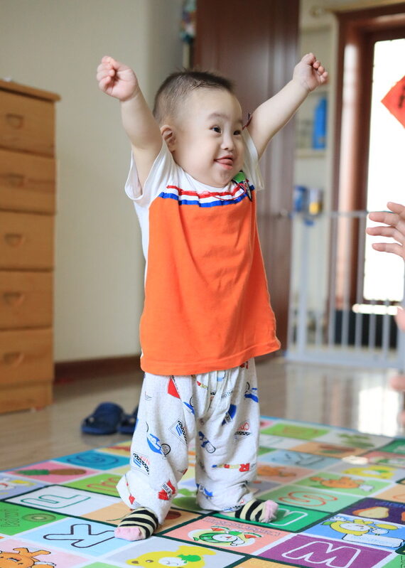 Baby boy with Down syndrome standing with arms in the air