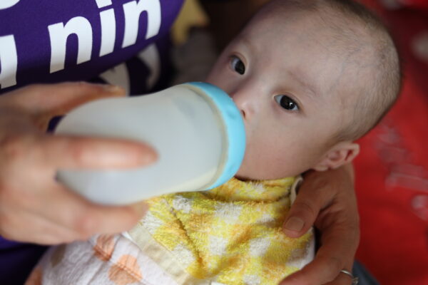 Baby in a yellow bib drinking from a bottle