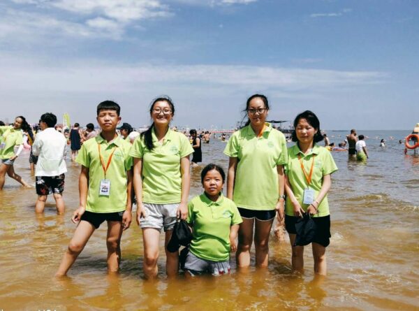 Five teens in matching green shirts stand in water on a crowded beach 20 Years of Hope