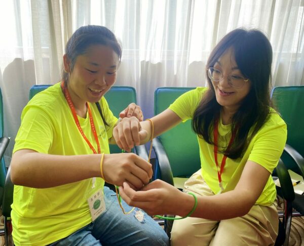 Two girls in matching fluorescent green shirts make friendship bracelets