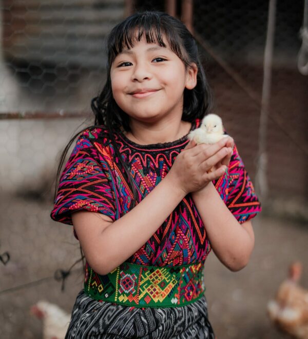Girl in traditional Guatemalan clothing holds a yellow baby chick