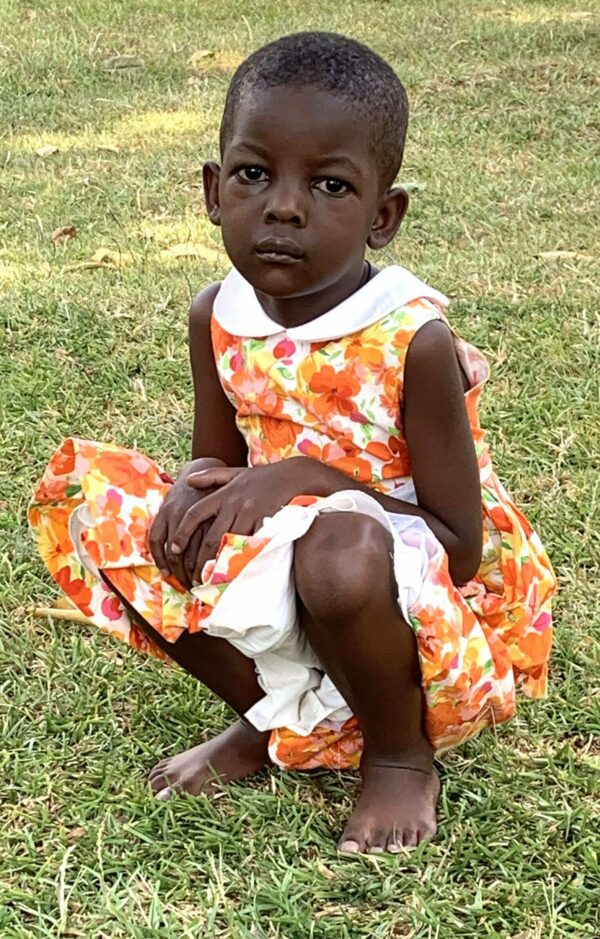 Young serious girl squatting in an orange and yellow flowered dress