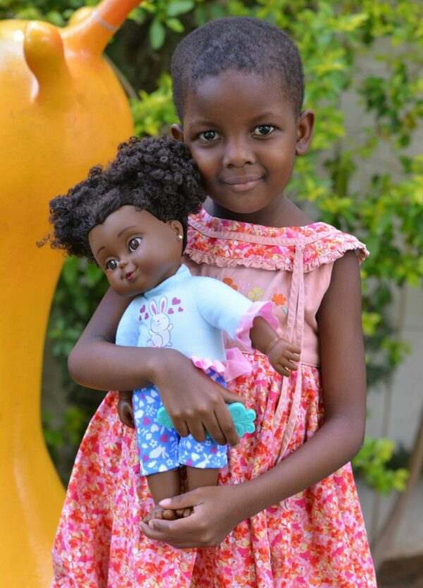 Young girl in a pink and orange dress holding a doll in Uganda