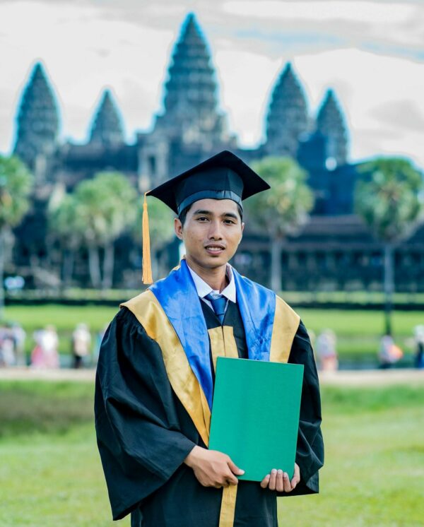 Man in graduation cap and gown standing in front of Angkor Wat in Cambodia