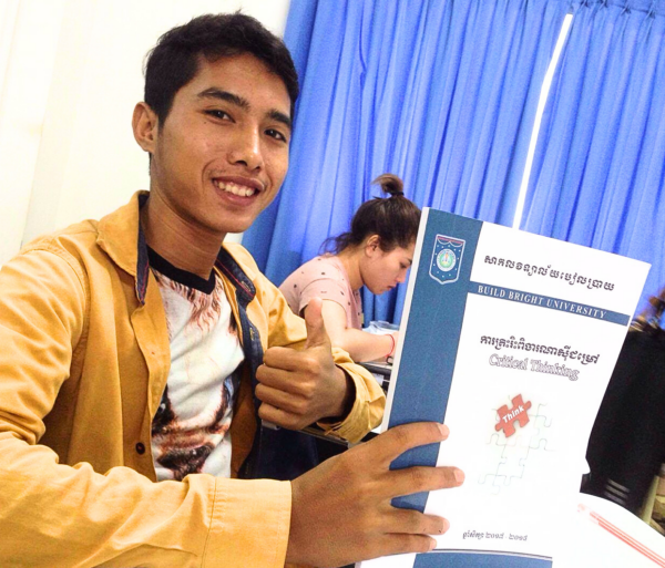 College student in a gold shirt holding a brochure from Build Bright University