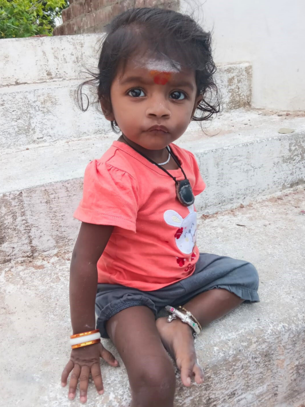 Little girl in coral shirt sits on a cement step in India