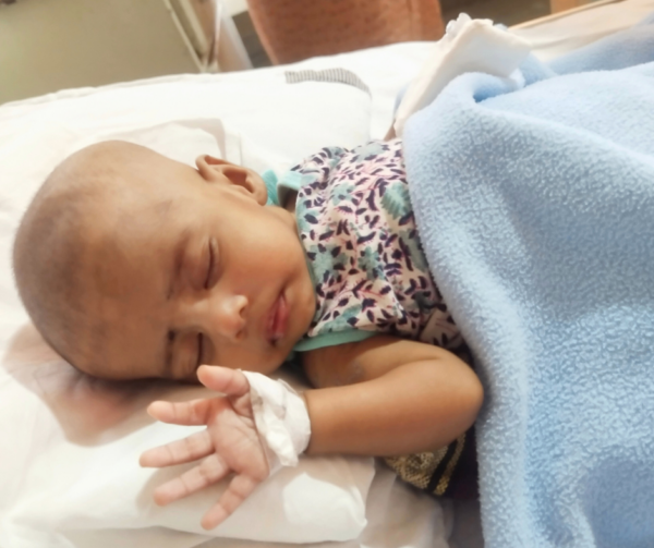 Baby lying in hospital bed in India with bandage on hand waiting for heart surgery