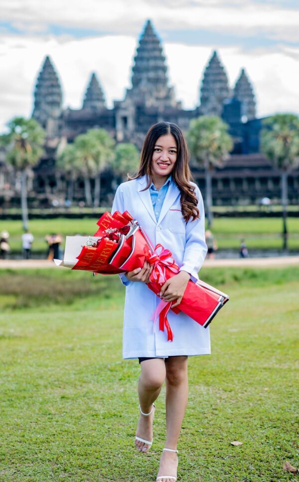 Young woman in pharmacy lab coat holding flowers in front of Angkor Wat