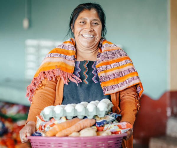 Guatemalan woman in orange holding a basket of food supplies