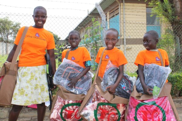 Four girls in orange shirts receive blankets and backpacks