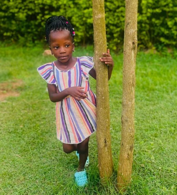 Ugandan girl in striped dress stands by a tree