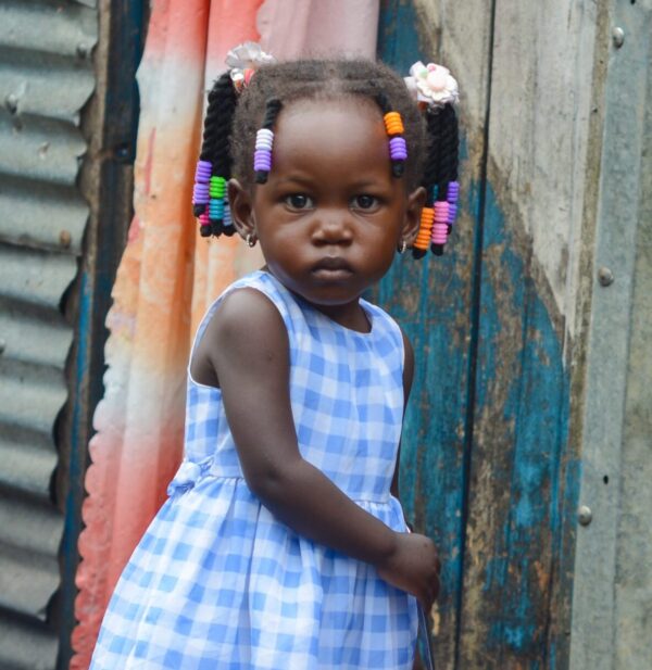 Young Ugandan girl in braids and a blue gingham dress waiting for cardiac surgery