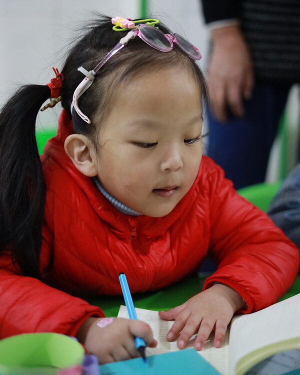 Young girl in red jacket writing at school