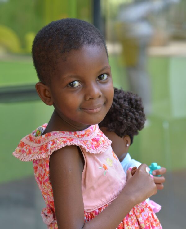 Young Ugandan girl in a pink and orange dress holding a doll