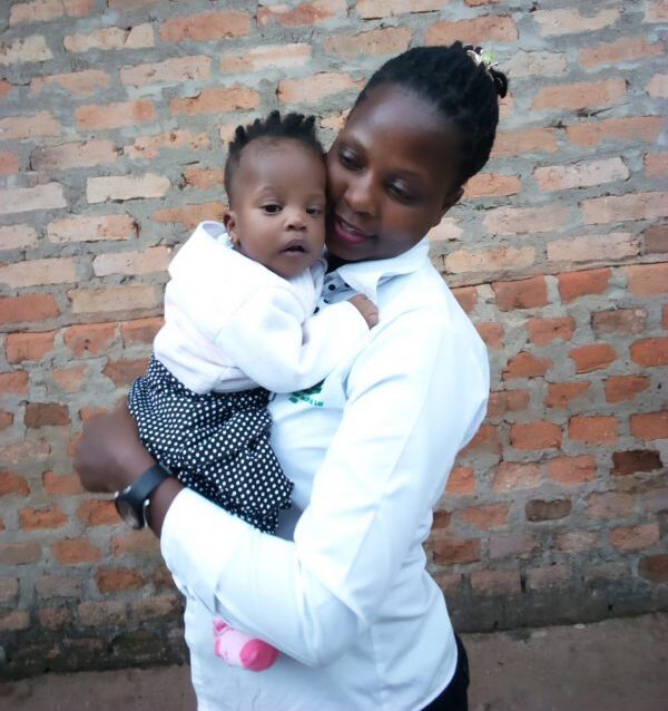 Mom and baby both in white standing in front of a brick wall
