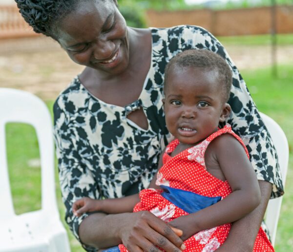 Toddler in red clothes sitting on his mom's lap in Uganda