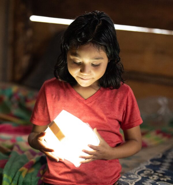 Girl in red shirt holds a glowing solar light in Guatemala