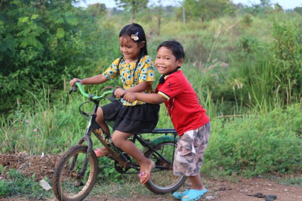 A brother helps his sister ride a bike