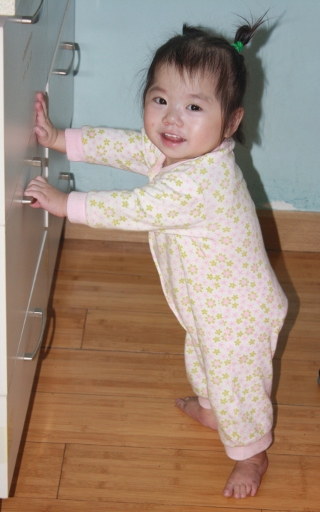 Toddler girl standing up holding onto a drawer