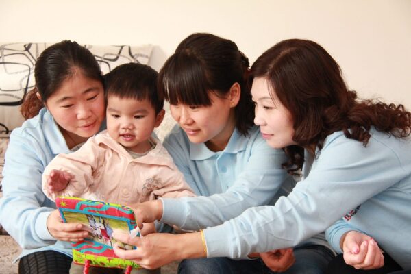 Three nannies from a China Healing Home showing a book to a little girl