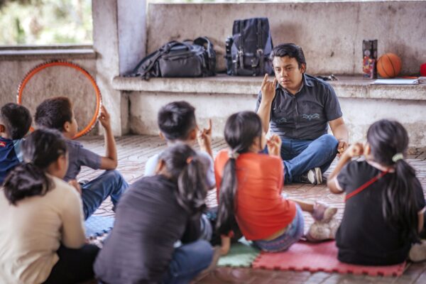 Man teaching sign language to a group of children sitting on the floor