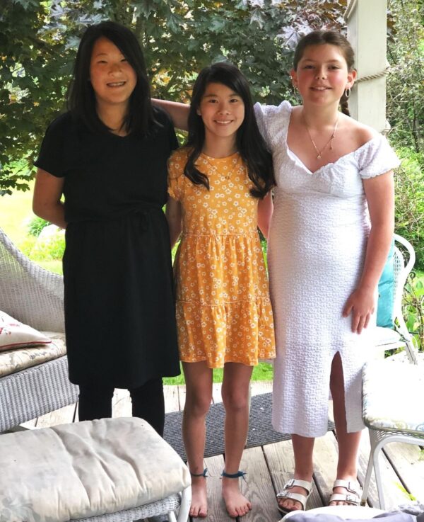 Three sisters wearing dresses stand on a patio