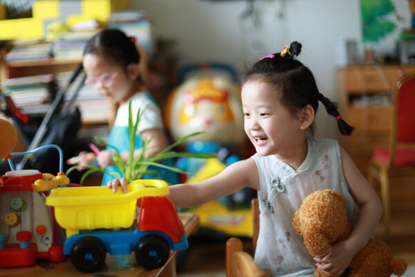 Little girl in pigtails playing with a truck and stuffed animal