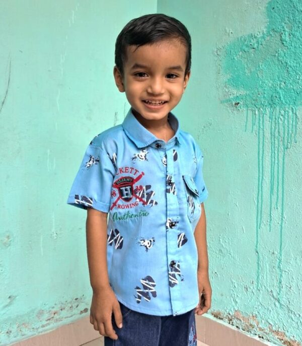 Young boy in blue standing in front of a turquoise wall