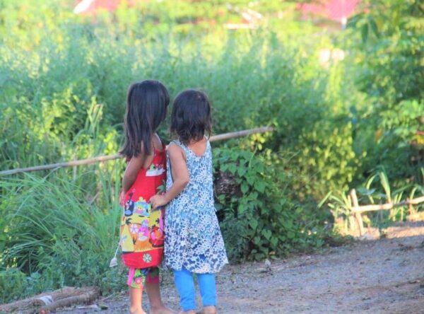 Two girls stand together looking away in rural Cambodia