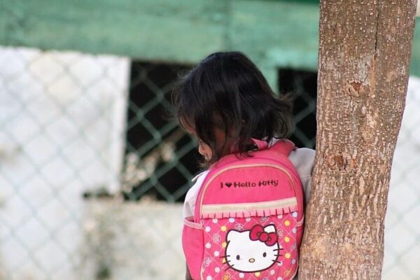 Little girl with a Hello Kitty backpack leans against a tree