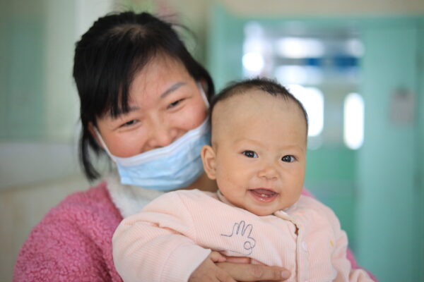 Mom wearing mask holds baby after baby had surgery through LWB's Unity Initiative