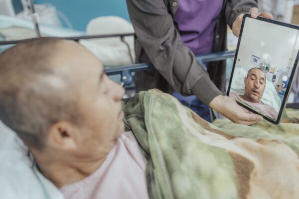 Man lying in hospital bed looks at his face on a tablet post cleft surgery