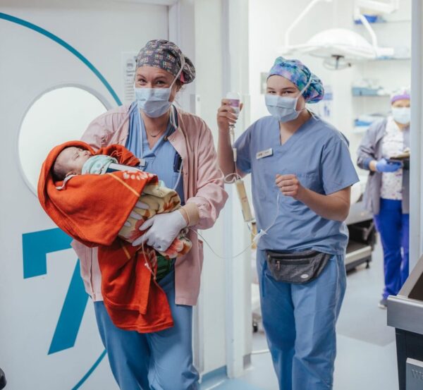 Two women taking a baby to the OR