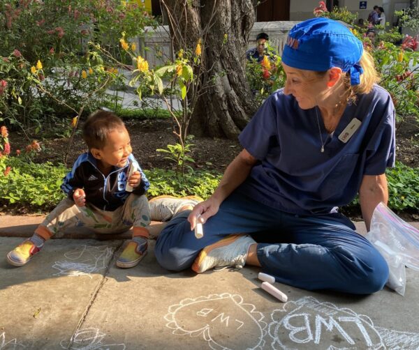 Cleft surgery volunteer sitting on sidewalk with child playing with chalk